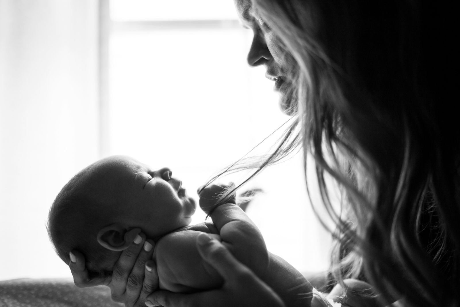 A mother cradling her newborn by a sunlit window
